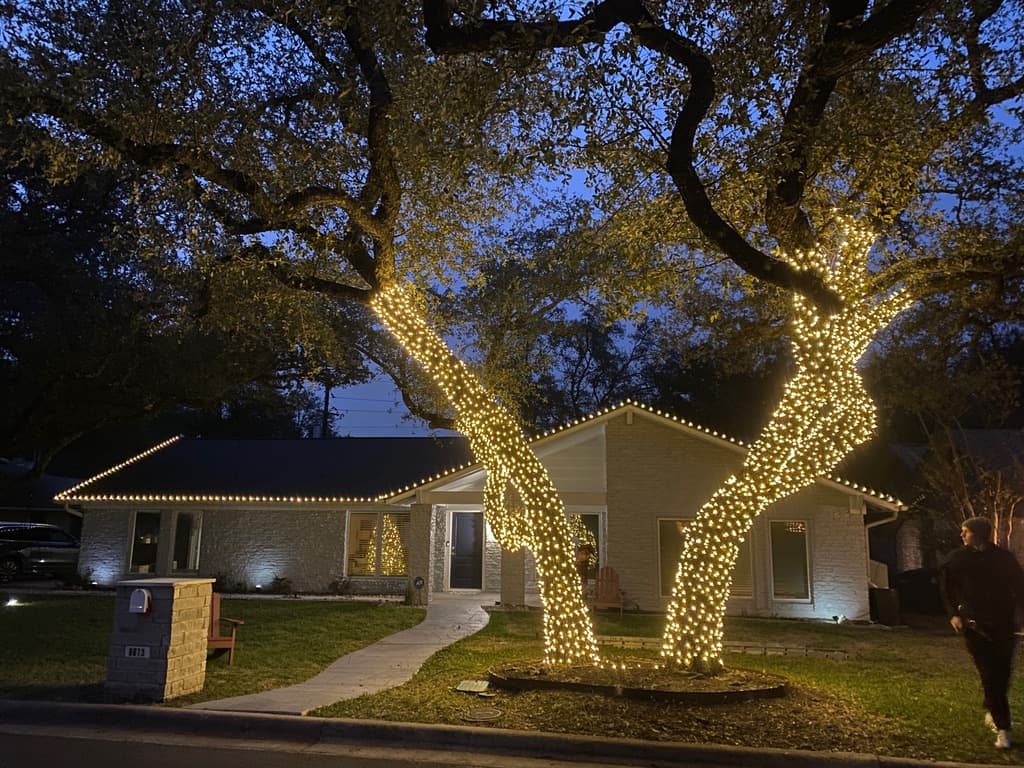 Austin home with a full warm-white roofline and two large fully-wrapped trees