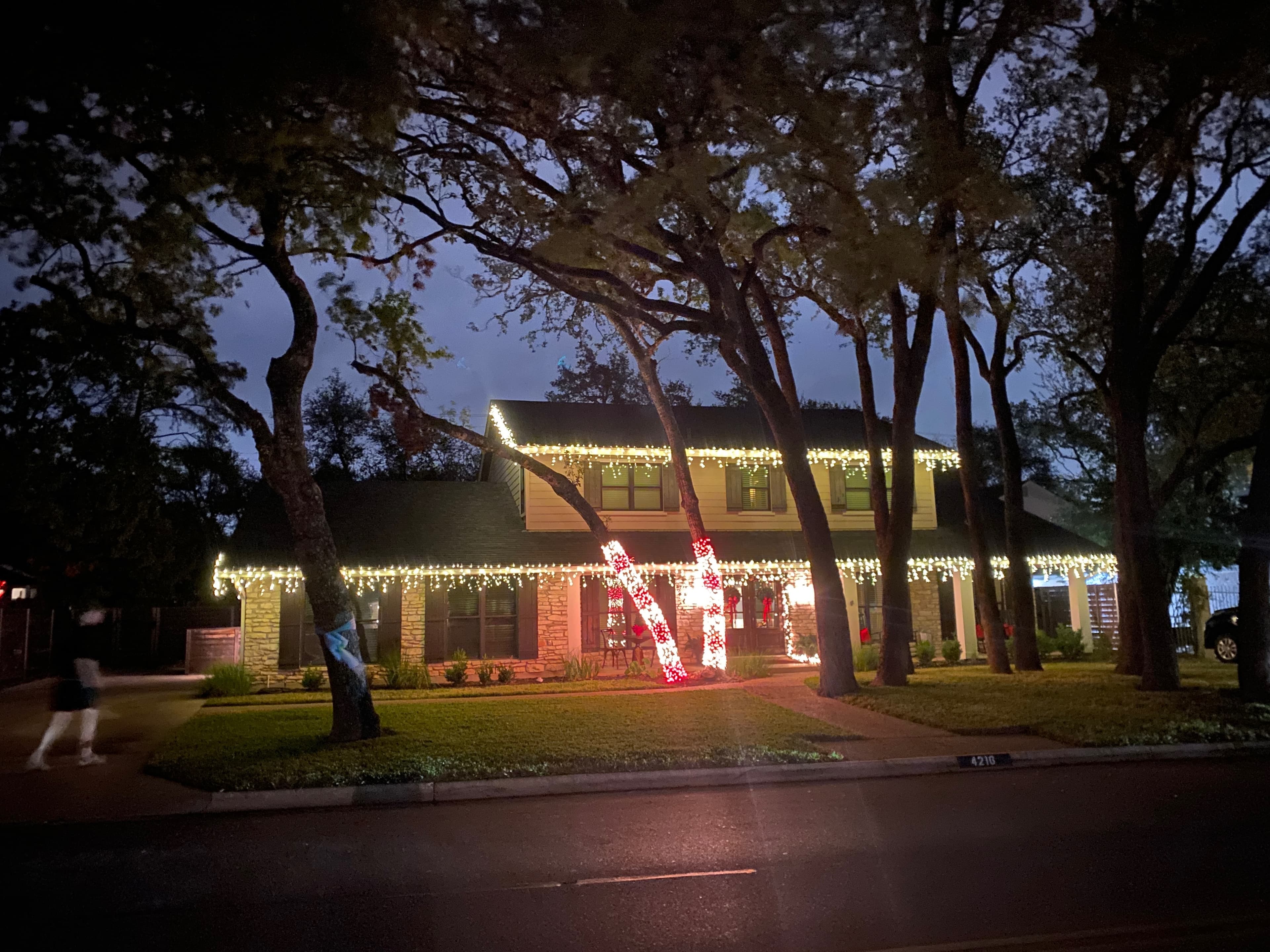 Two-story home with icicle roofline lights and two candy-cane-style wrapped trees